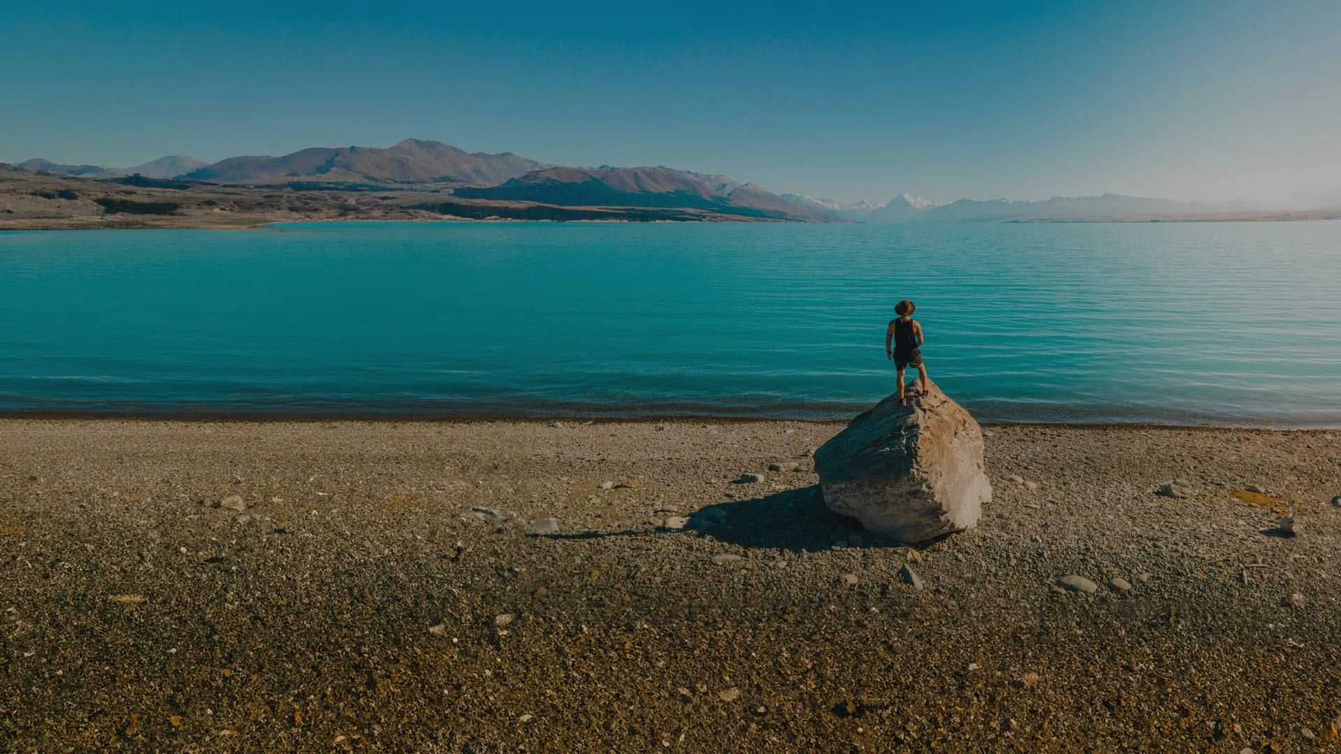 Man standing on a rock on the shore of Lake Tekapo