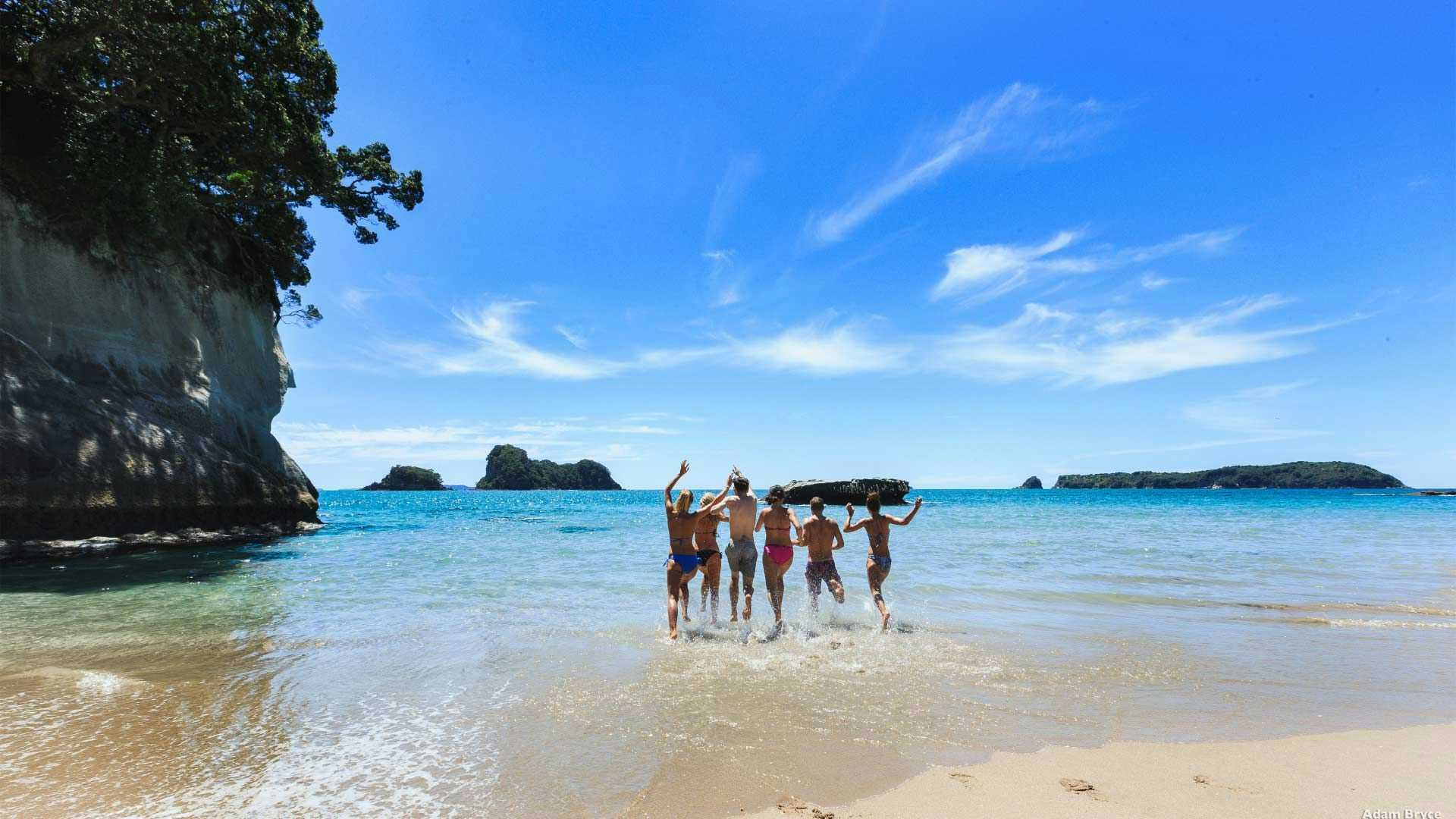 Group of friends run into the ocean at the Coromandel in New Zealand